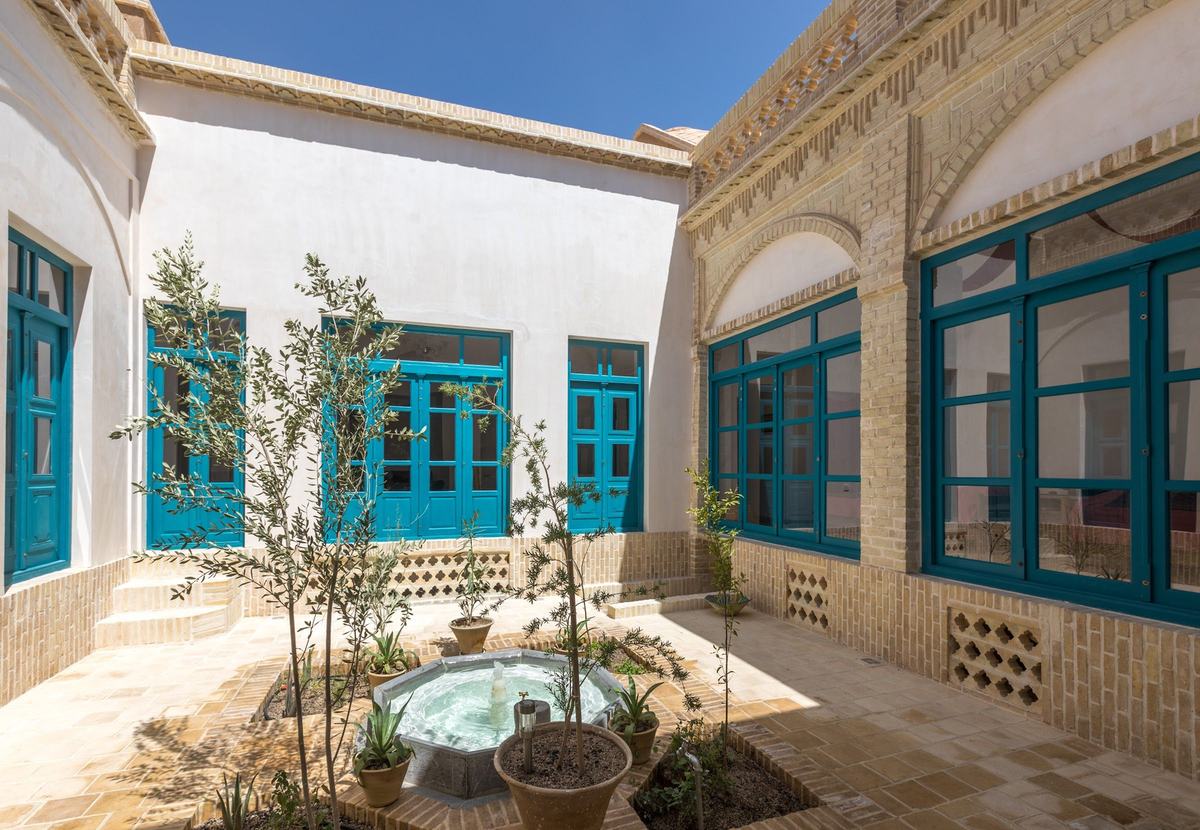 The courtyard of Lari House: a small octagonal fountain, young olive trees and turquoise windows in white walls and yellow brick