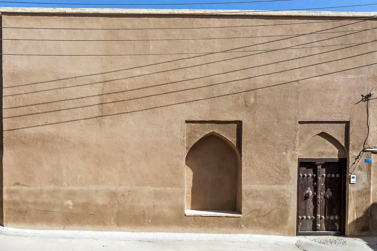 The street front: a long earthen wall with a pointed alcove and an old studded wooden door
