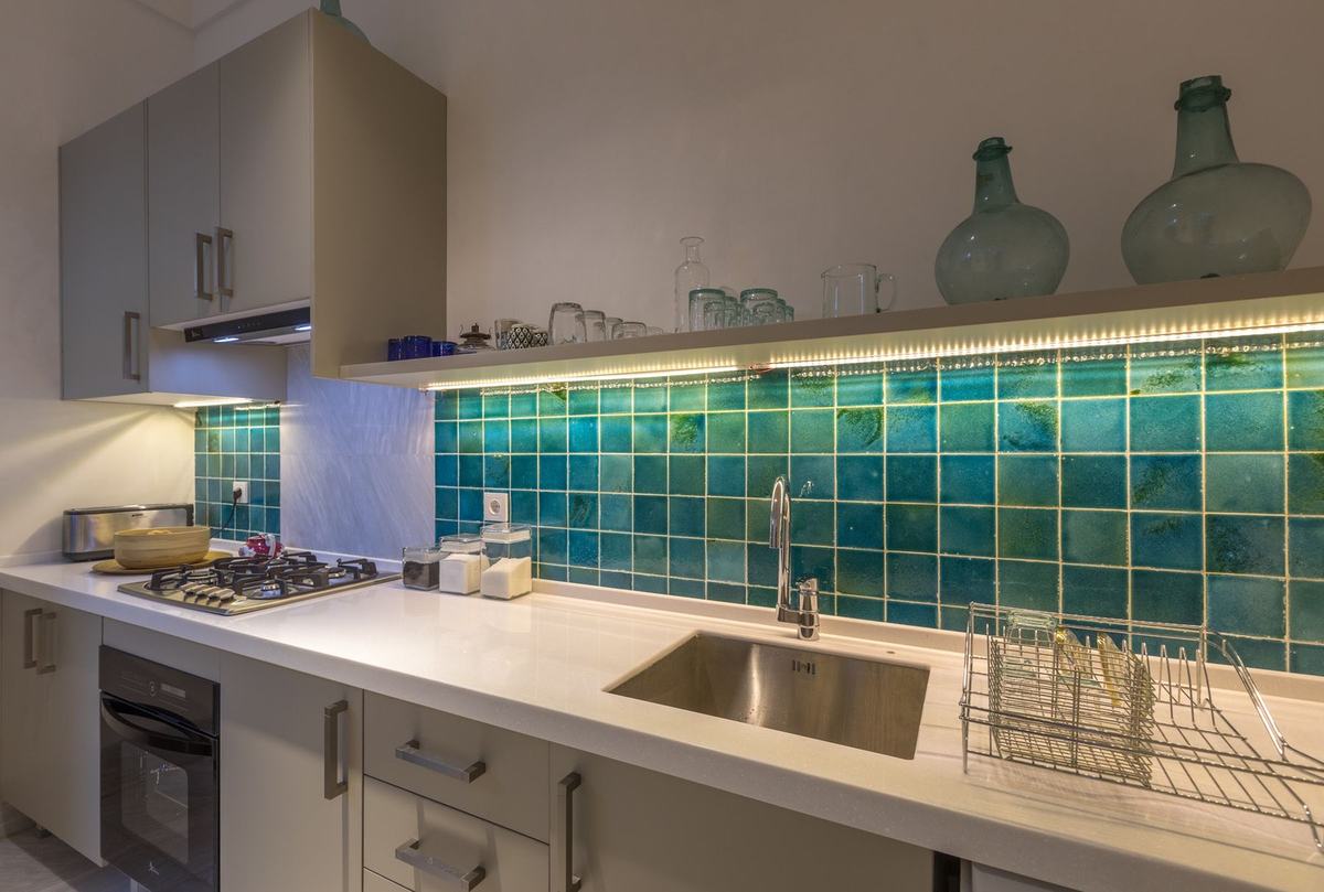 The house kitchen: hand-glazed turquoise tiles, a white counter and glass jars on an open shelf