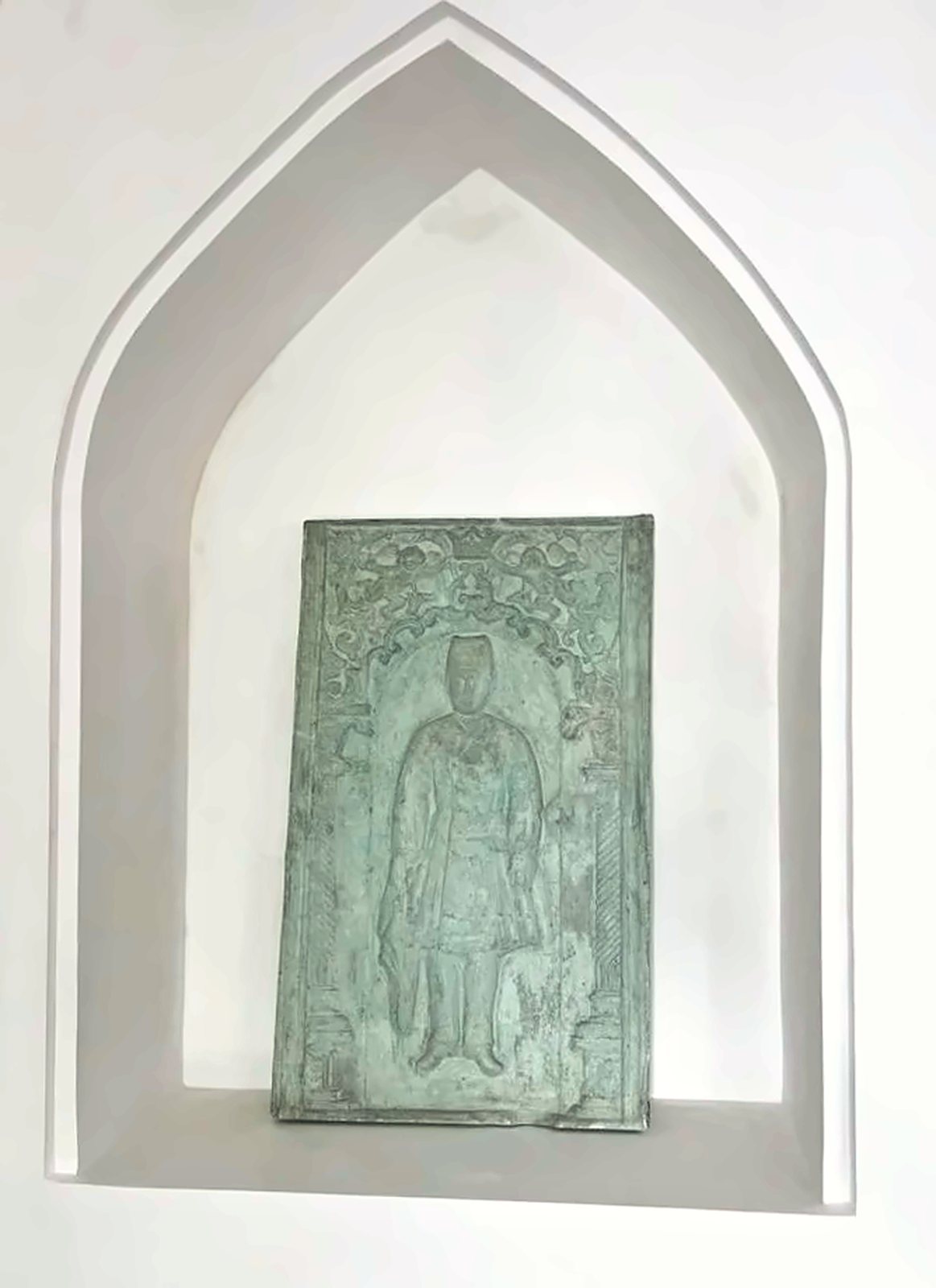 A carved relief panel of a standing figure set in a pointed white niche