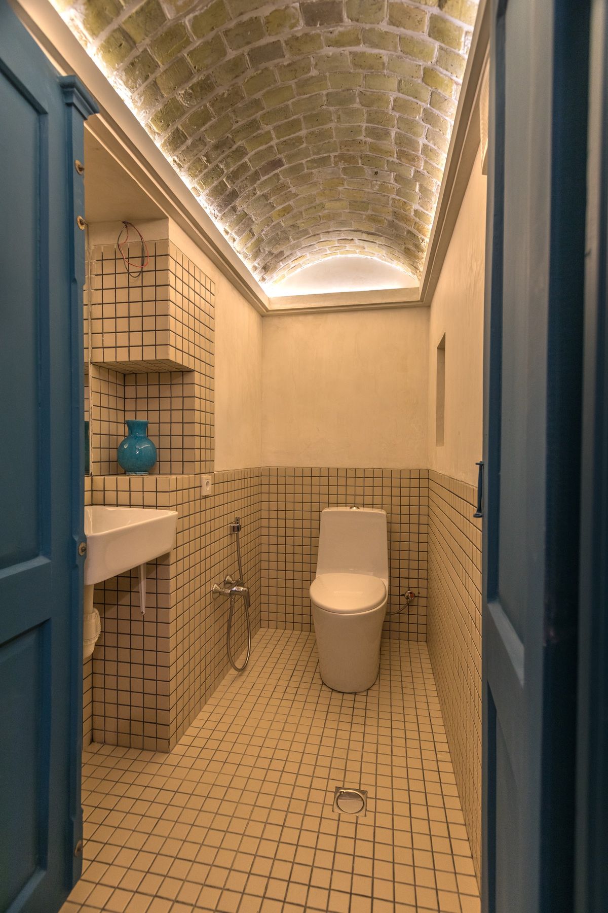Sardab's own toilet: a lit brick vault above cream tiles and a turquoise vase in a niche