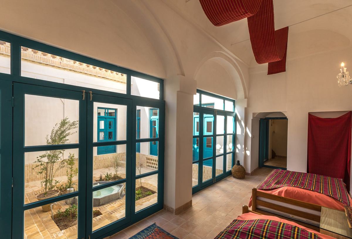 Talar: single beds under a long vault, tall turquoise windows onto the courtyard